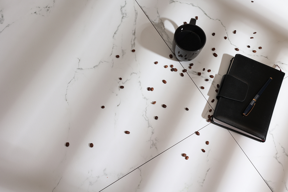 Мраморный пол с кофейными зернами, кружкой и записной книжкой. Белый мраморный пол с кофе, зернами и черной записной книжкой.