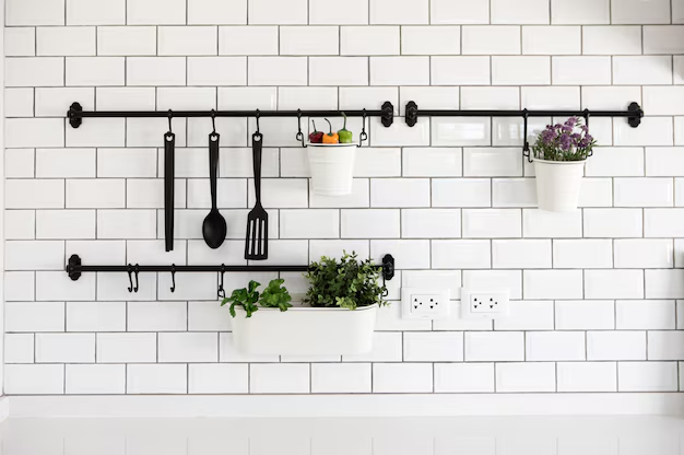 Кухонная полка с кухонными принадлежностями и растениями на белой кирпичной стене. Кухонная полка с черными крючками на фоне белой кирпичной стены.